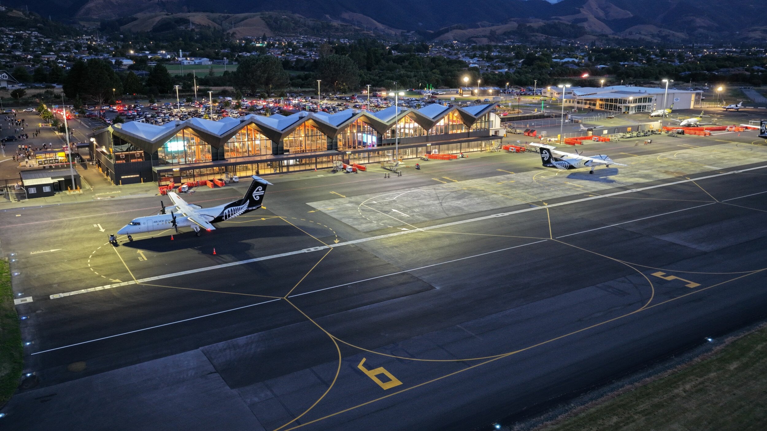 The Nelson Airport apron at night with the terminal lit up behind it. Two Air NZ aircraft are parked on the apron.