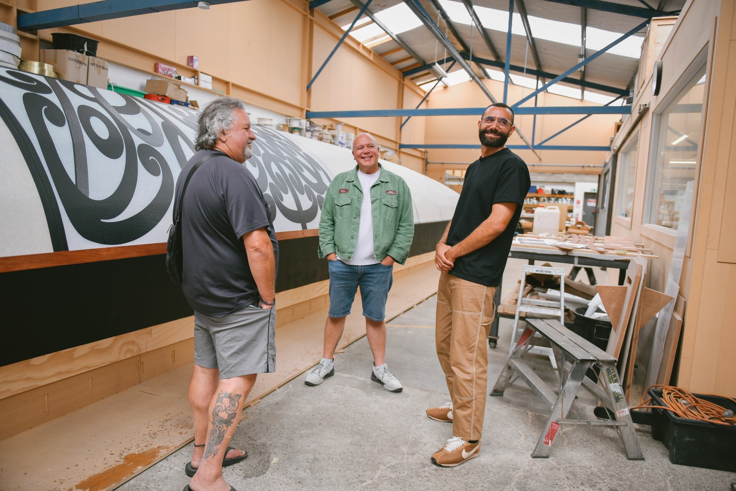 Fayne Robinson, Rōpata Taylor and Tyrone Ohia stand beside the half-finished waka in a workshop