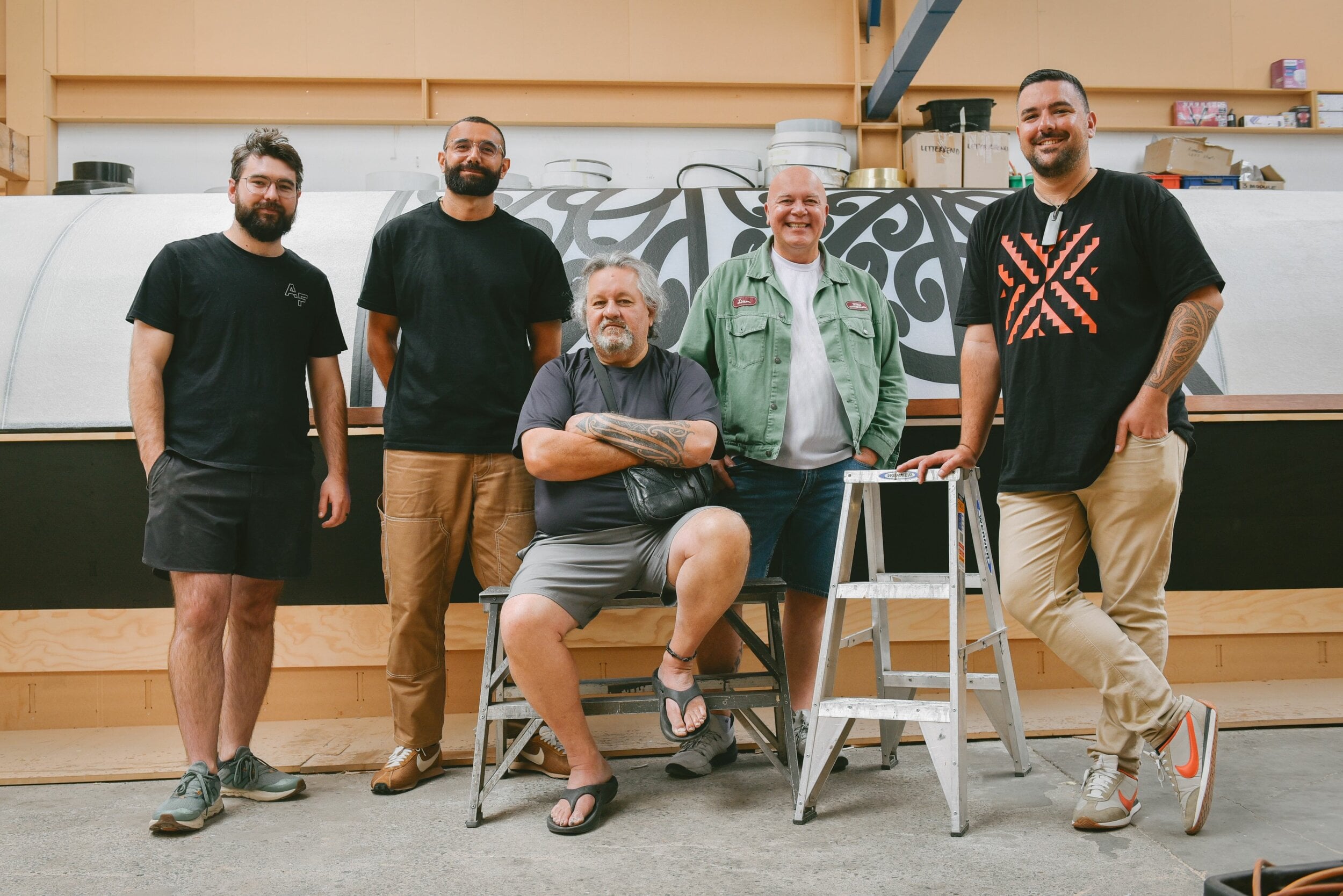 Project team Ben Lakin, Tyrone Ohia, Fayne Robinson, Rōpata Taylor and Johny O'Donnell pose in front of the half-completed waka in a workshop.