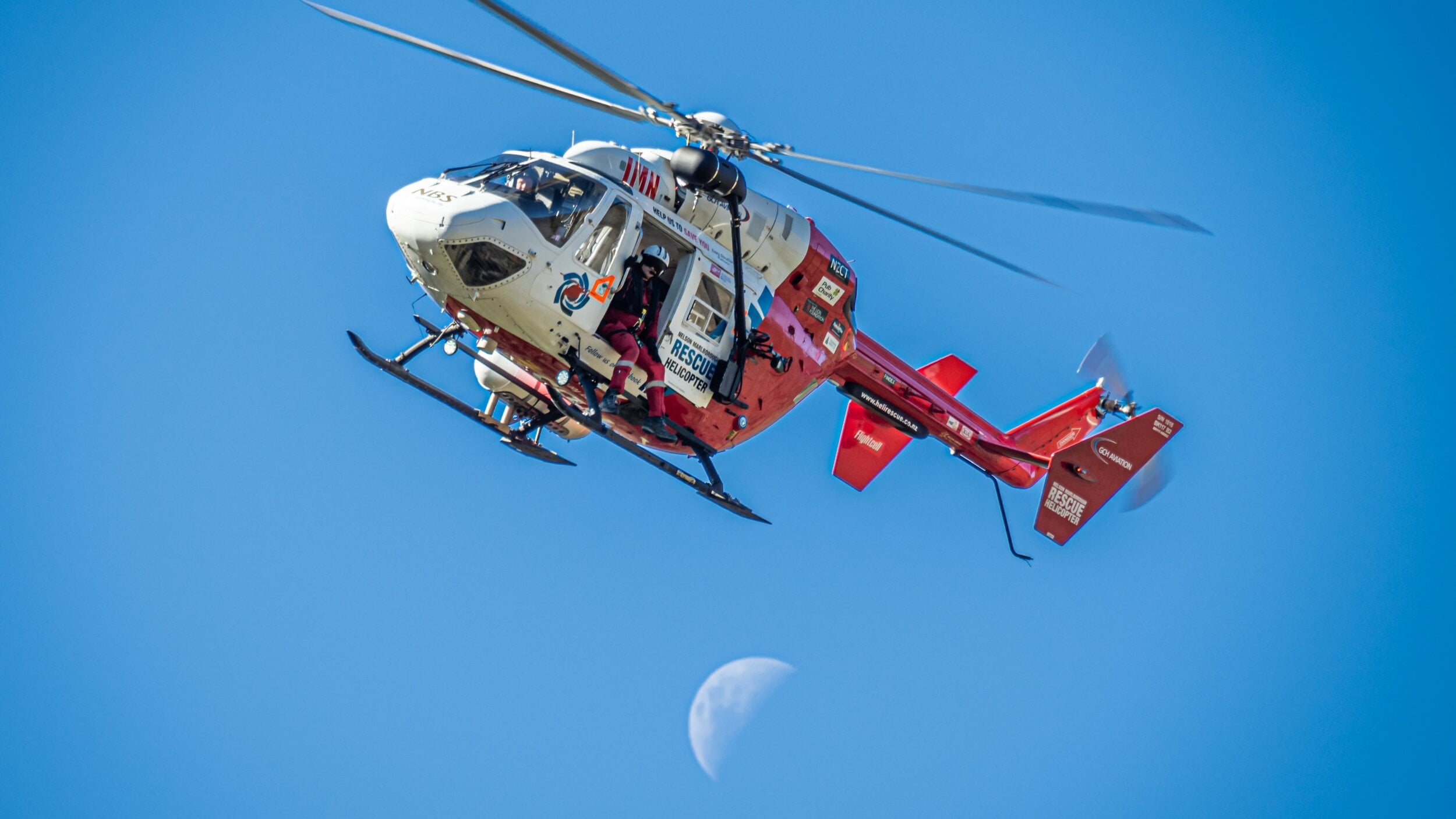 The Nelson Marlborough Rescue Helicopter flies against a blue sky.